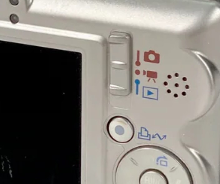 Canon IXUS 55 löystynyt kuvausmoodin valitsin takakuoren kulmassa.